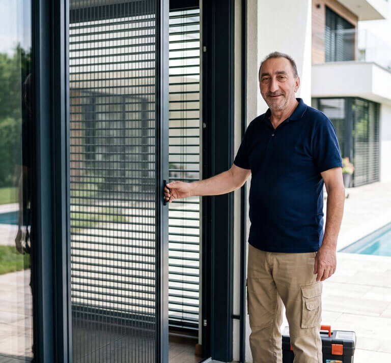 Majstor pokazuje plise komarnik na velikim staklenim balkonskim vratima pored moderne kuće sa bazenom.
